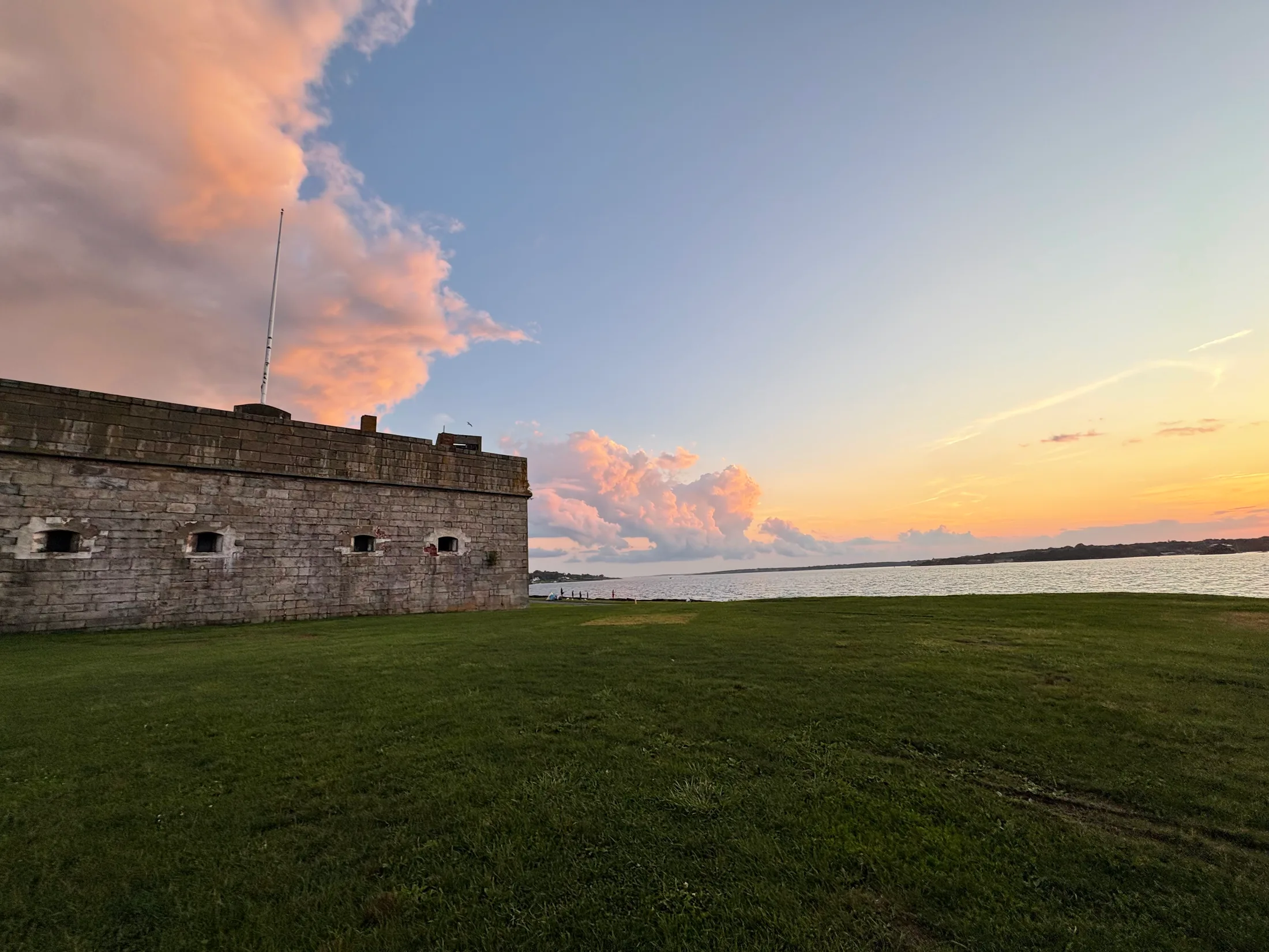 Fort Adams’ waterfront walls and lawn beneath pink clouds at sunset