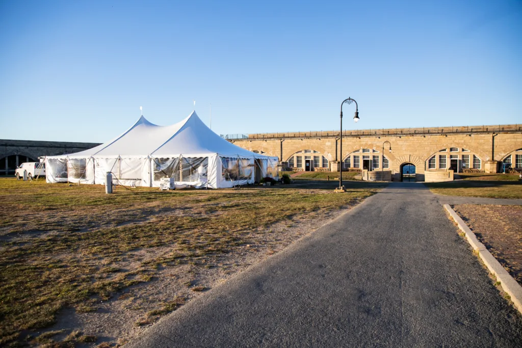 A white event tent set against the historic walls of the Parade Field at Fort Adams